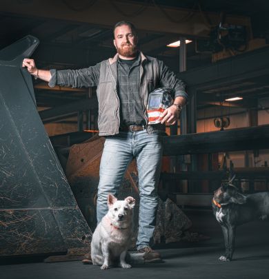 Person standing next to welding equipment and two dogs