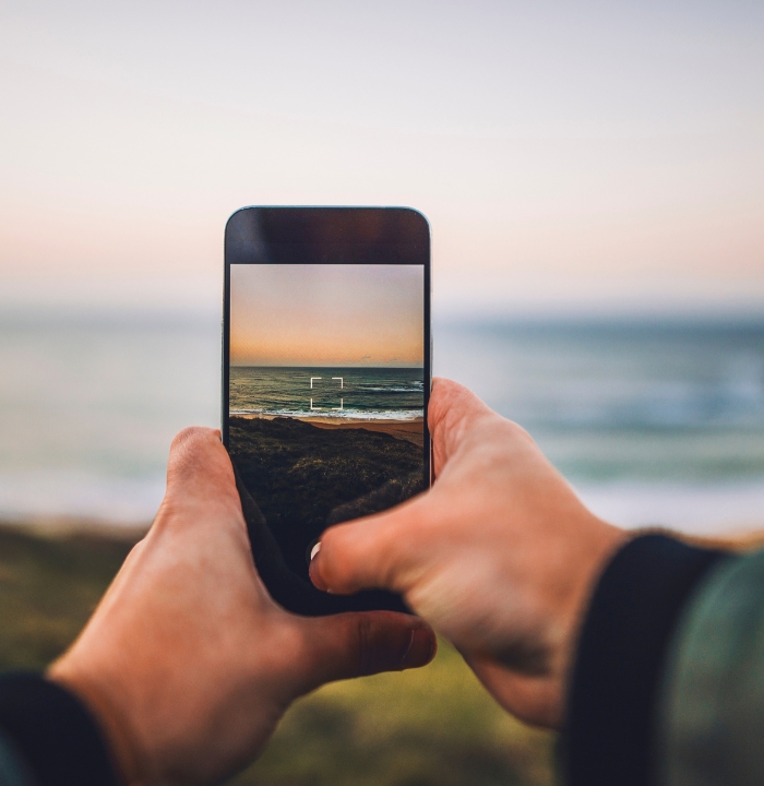 Hands holding phone and taking photo of beach
